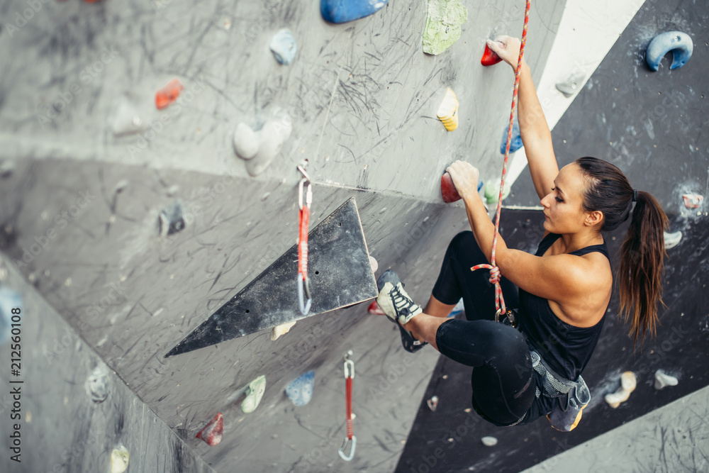 Beautiful young woman in black outfit climbing on practical wall in gym, bouldering, extreme sport, rock-climbing concept. - obrazy, fototapety, plakaty 