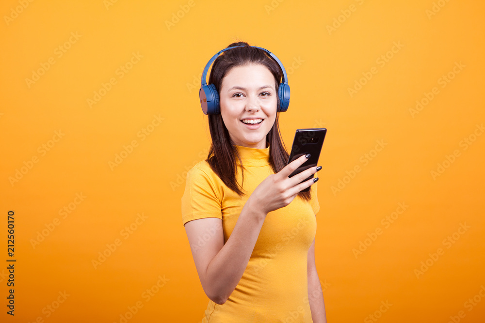 Cute young woman texting on her phone while listening music,while listening music on yellow background Cute young woman texting on her phone while listening music,while listening music on yellow background