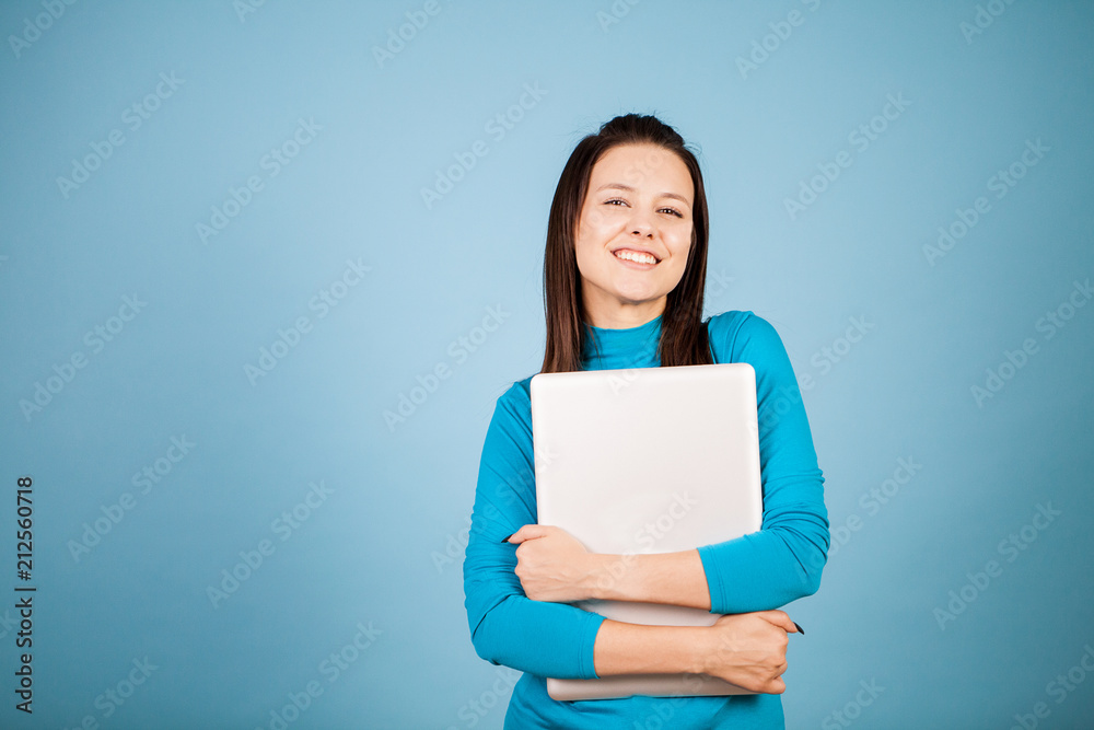 Young studing holding her laptop in her arms in studio on blue background Young studing holding her laptop in her arms in studio on blue background