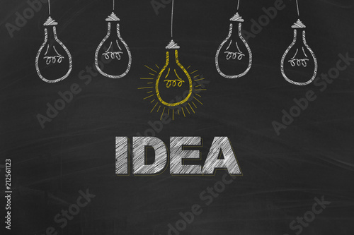 Idea written with chalk on board plus light bulbs in front of black blackground