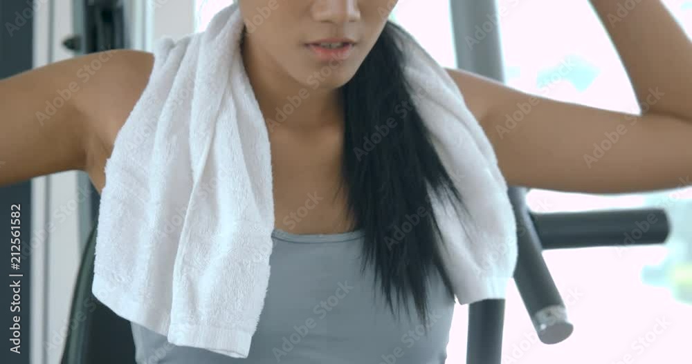 Attractive asian girl body builder using a weights machine in the gym.