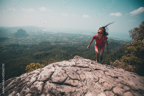 woman backpacker running up on mountain top cliff edge photo