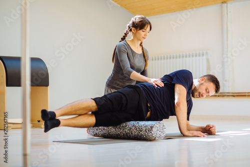 Fotografie Female coach rehabilitation specialist helping young handsome man doing exercise with side surface shin