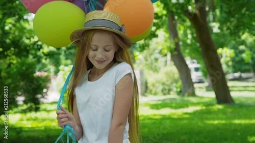 Portrait of pretty girl poses at camera with colourful balloons in sunny park