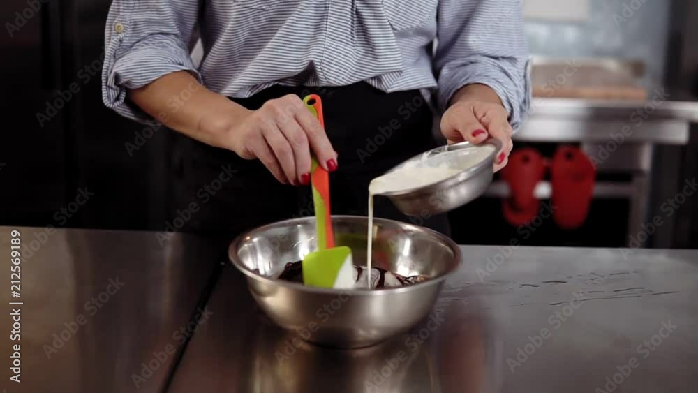 Woman in darl apron is mixing the ingredients of a cake in a stainless bowl in her kitchen pouring cream. Culinary, kitchen concept Woman in darl apron is mixing the ingredients of a cake in a stainless bowl in her kitchen pouring cream. Culinary, kitchen concept