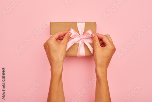 Hands tying pink bow on a present box © ArtFamily