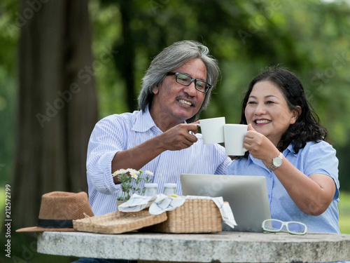 Senior couple looking laptop and have breakfast in the garden together.