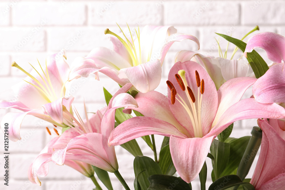 Fototapeta premium Beautiful blooming lily flowers on brick wall background