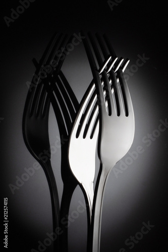 Fotografie Two interlocking shiny forks on reflective black background for artistic minimalist still life