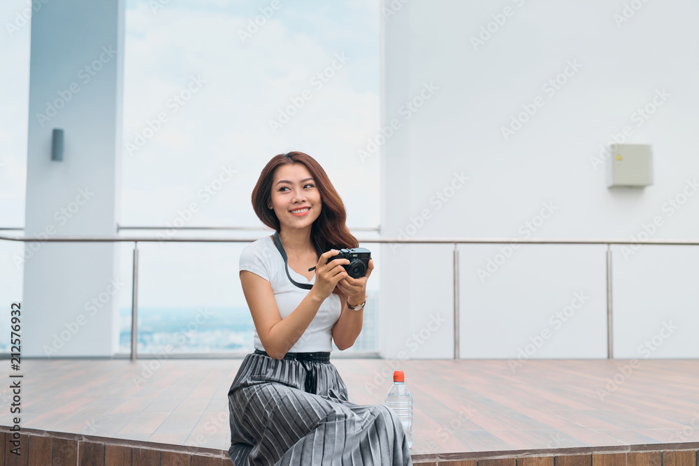 Beautiful asian woman sit at the edge of street, smiling with camera in hand, travel concept.