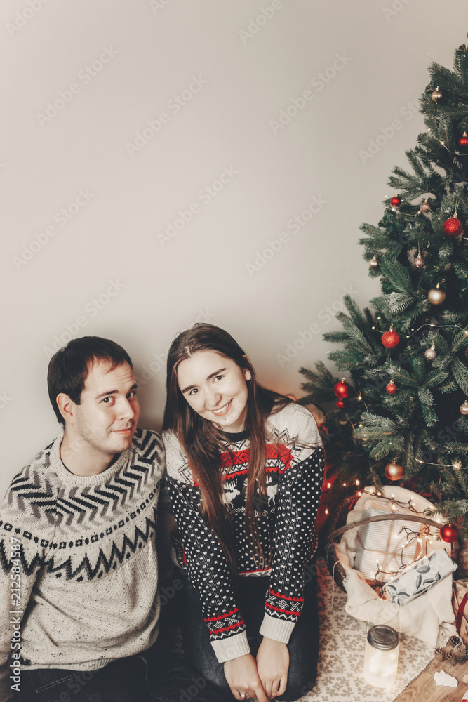 stylish hipster couple in sweaters hugging and embracing at christmas tree in cozy evening room. atmospheric moments. merry christmas and happy new year concept. happy holidays stylish hipster couple in sweaters hugging and embracing at christmas tree in cozy evening room. atmospheric moments. merry christmas and happy new year concept. happy holidays