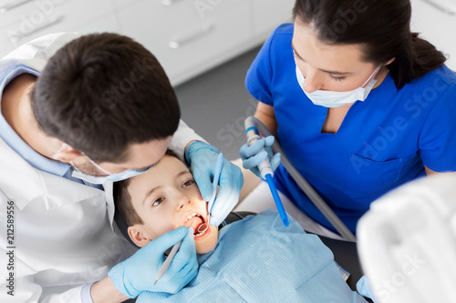 medicine  dentistry and healthcare concept - dentist with mouth mirror and probe checking for kid patient teeth at dental clinic