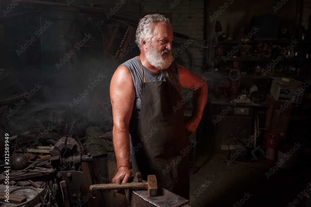 Portrait of a blacksmith artisan in an apron with an anvil in a blacksmith Portrait of a blacksmith artisan in an apron with an anvil in a blacksmith