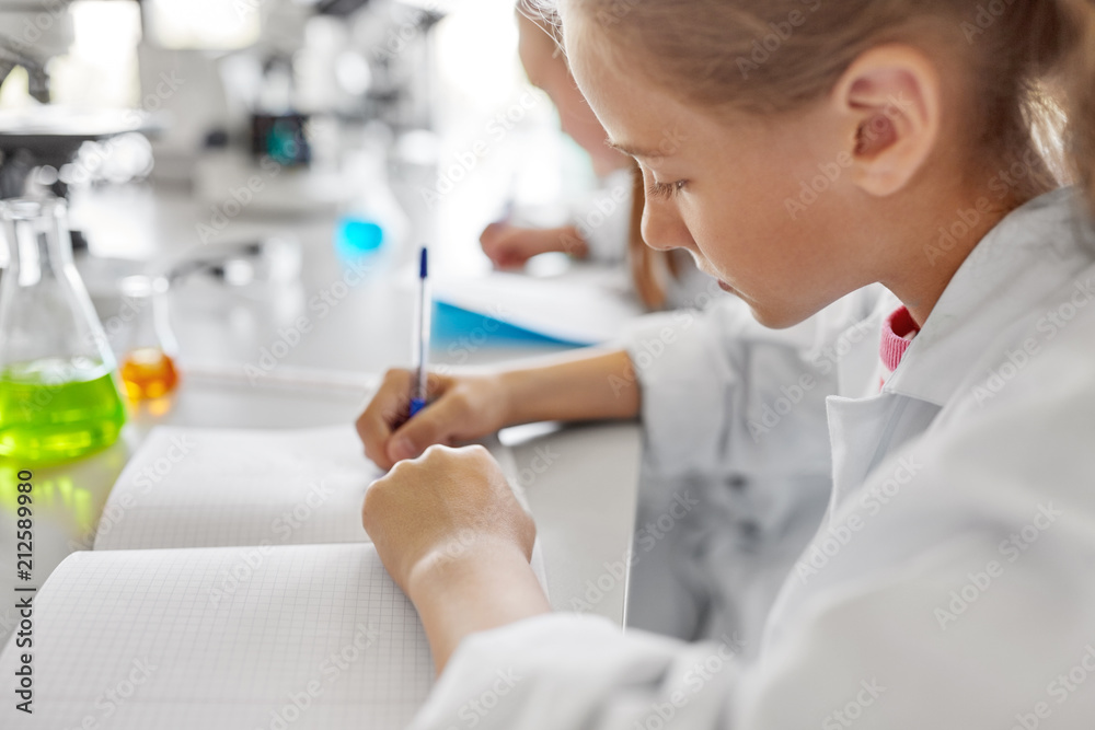 education, science and children concept - close up of girl studying chemistry at school laboratory and writing to workbook education, science and children concept - close up of girl studying chemistry at school laboratory and writing to workbook