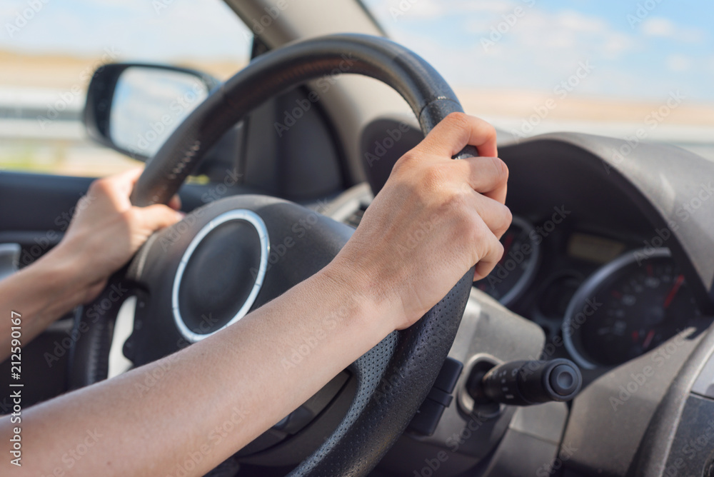 Female hands on the steering wheel of a car while driving