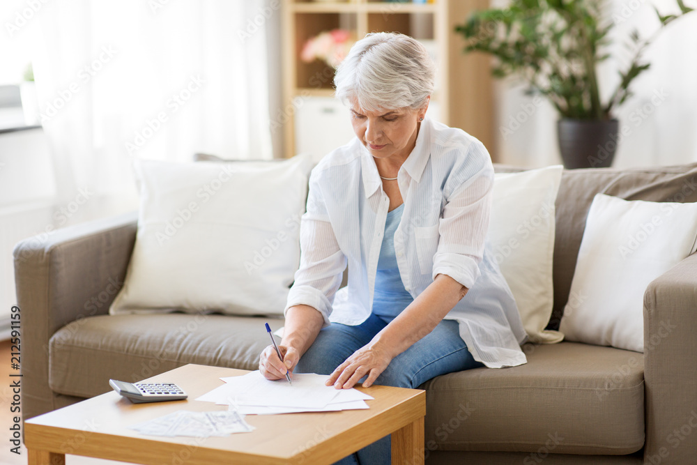 business, savings, annuity insurance, age and people concept - senior woman with papers or bills and calculator writing at home business, savings, annuity insurance, age and people concept - senior woman with papers or bills and calculator writing at home