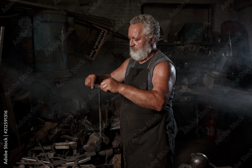 Brutal blacksmith artisan in apron makes the product in the blacksmith Brutal blacksmith artisan in apron makes the product in the blacksmith