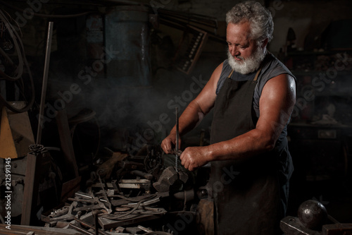 Brutal blacksmith artisan in apron makes the product in the blacksmith