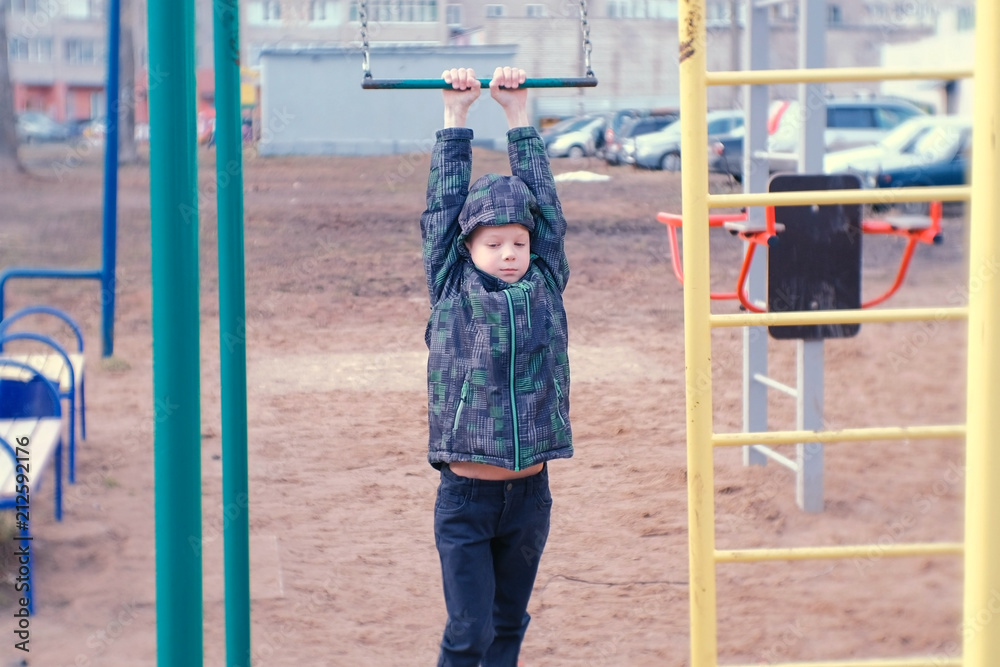 Obraz premium Boy swings on a gymnastic trapeze, jumps and fall on sand. Playground in the courtyard of the city house.
