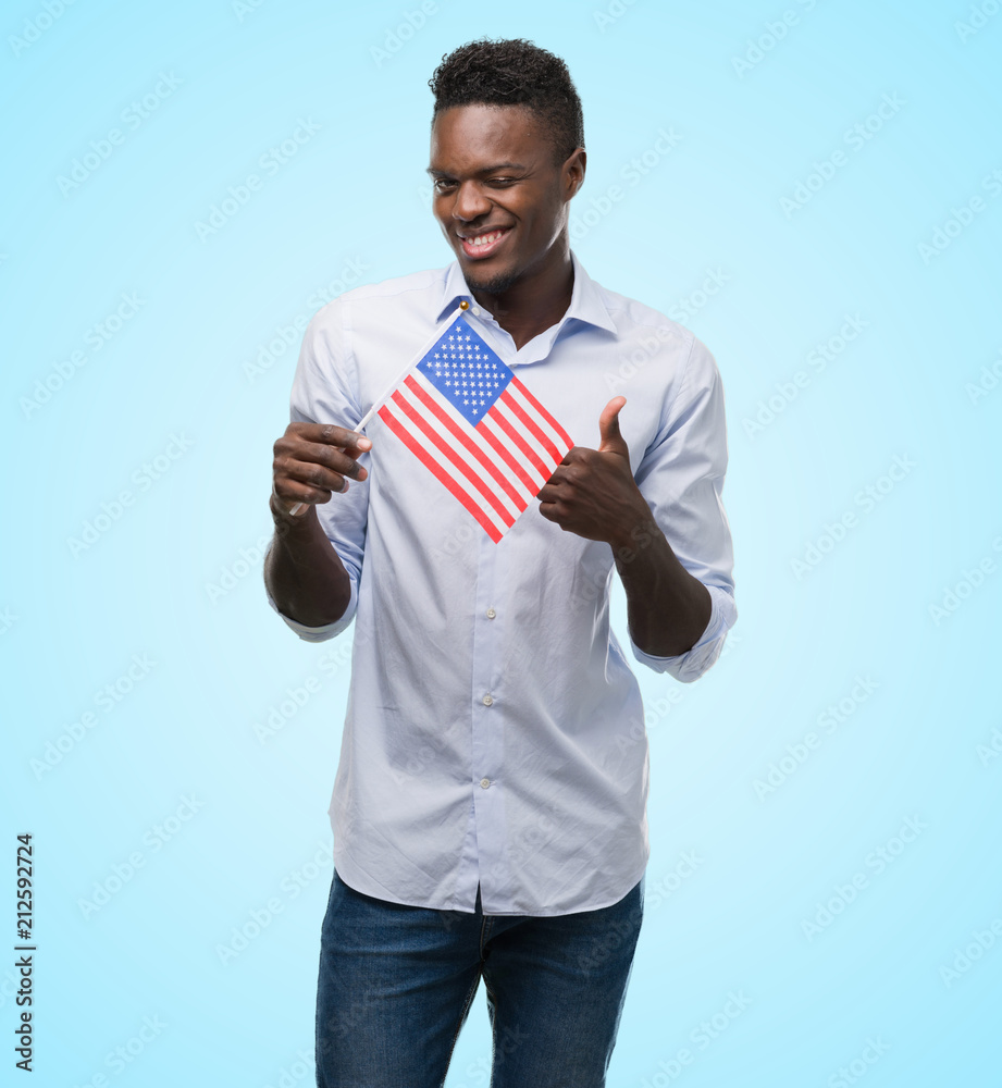 Young african american man holding USA flag happy with big smile doing ok sign, thumb up with fingers, excellent sign Young african american man holding USA flag happy with big smile doing ok sign, thumb up with fingers, excellent sign