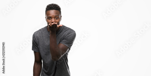 Young african american man wearing grey t-shirt looking at the camera blowing a kiss with hand on air being lovely and sexy. Love expression.
