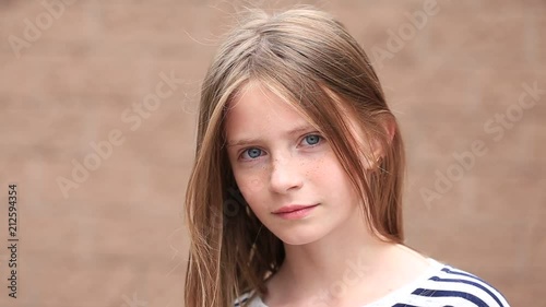 Beautiful blond young girl with freckles outdoors on wall background, close up portrait