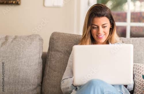 Young beautiful woman smiling using laptop on the sofa looking confident.