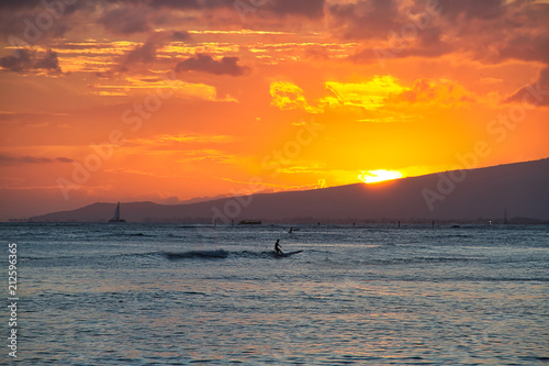 A man enjoying surfing off the coast of Oahu during sunset.