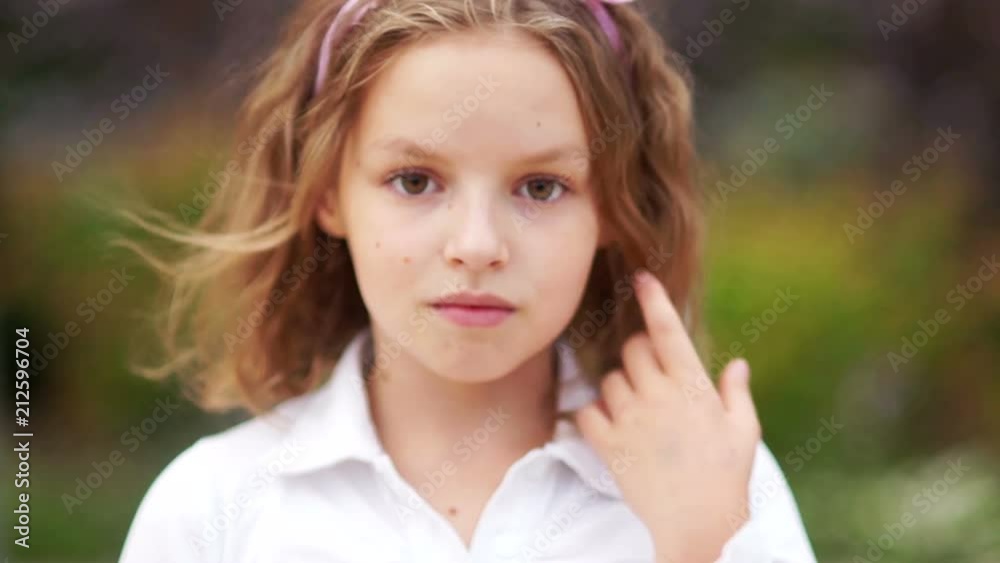 Closed portrait of a young schoolgirl. The girl calmly looks at the frame, straightens her hair. Curly hair, brown eyes, natural beauty Closed portrait of a young schoolgirl. The girl calmly looks at the frame, straightens her hair. Curly hair, brown eyes, natural beauty