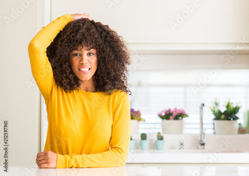 African american woman wearing yellow sweater at kitchen confuse and wonder about question. Uncertain with doubt, thinking with hand on head. Pensive concept.