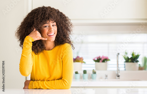 African american woman wearing yellow sweater at kitchen smiling doing phone gesture with hand and fingers like talking on the telephone. Communicating concepts.