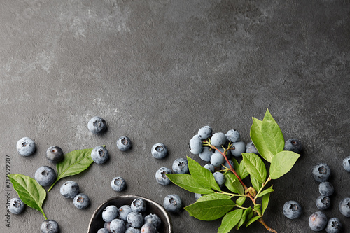 Fresh blueberries with leaves on branch. Black stone background, top view.