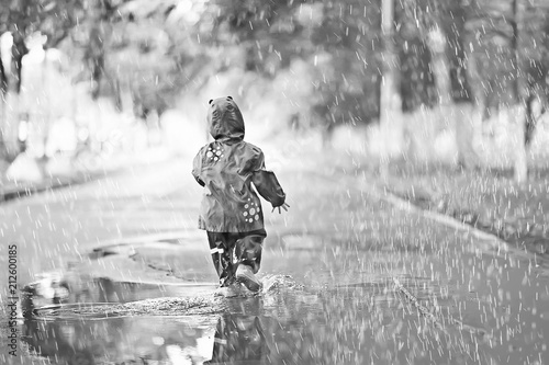cheerful little girl walks and jumps in puddles in the rain