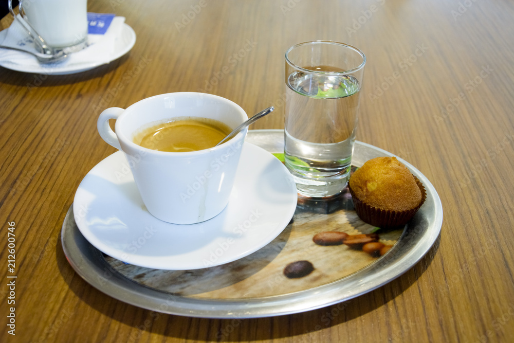 Cup of coffee with glass of water and a cookie in a iron plate.