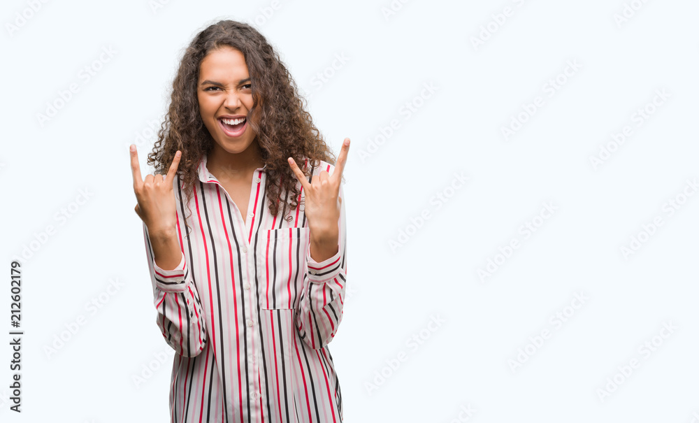 Beautiful young hispanic woman shouting with crazy expression doing rock symbol with hands up. Music star. Heavy concept. Beautiful young hispanic woman shouting with crazy expression doing rock symbol with hands up. Music star. Heavy concept.