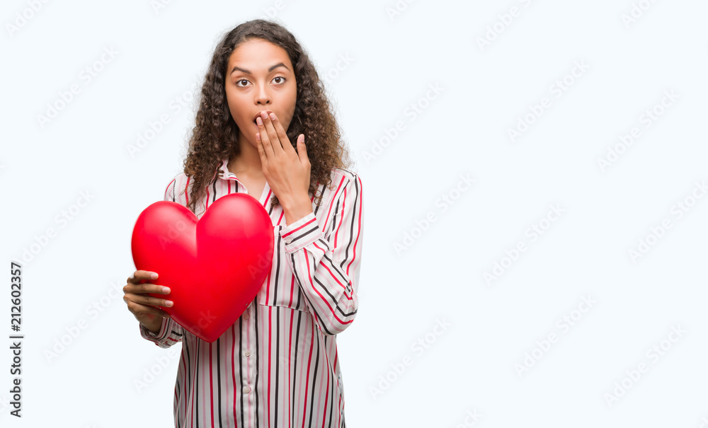 Young hispanic woman in love holding red heart cover mouth with hand shocked with shame for mistake, expression of fear, scared in silence, secret concept Young hispanic woman in love holding red heart cover mouth with hand shocked with shame for mistake, expression of fear, scared in silence, secret concept