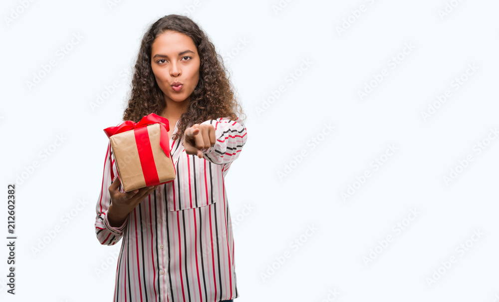 Young hispanic woman in love holding present pointing with finger to the camera and to you, hand sign, positive and confident gesture from the front Young hispanic woman in love holding present pointing with finger to the camera and to you, hand sign, positive and confident gesture from the front