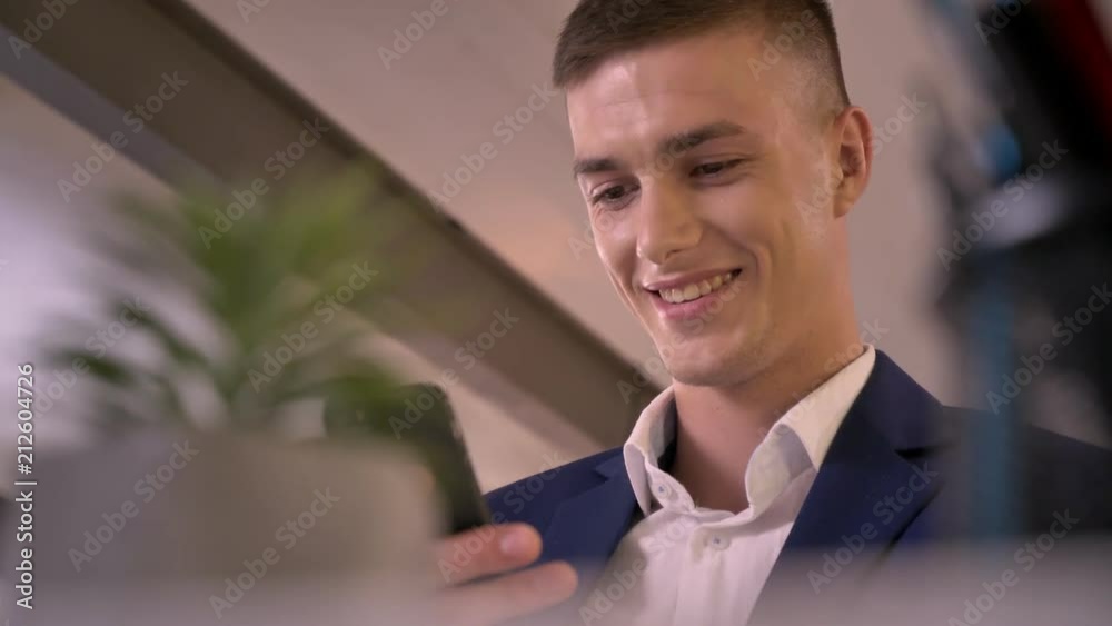 Young attractive businessman is holding smartphone in hand, smiling, communication concept, blurred foreground Young attractive businessman is holding smartphone in hand, smiling, communication concept, blurred foreground