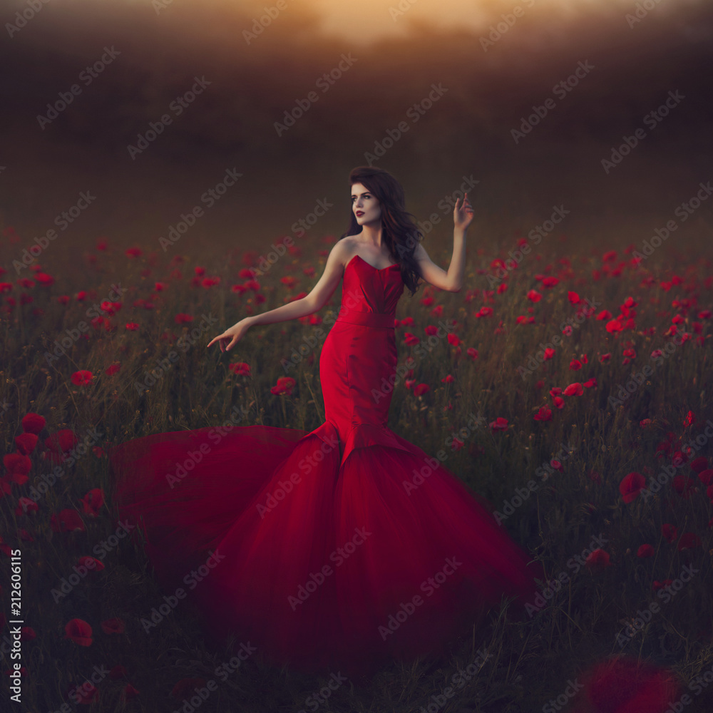 Beautiful girl in a posh red dress posing on a poppy field. Poppy field at sunset. Art processing.