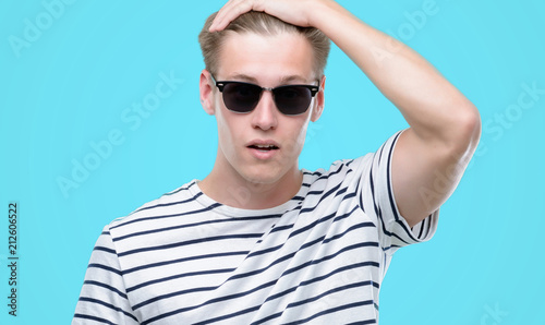 Young handsome blond man wearing sunglasess stressed with hand on head, shocked with shame and surprise face, angry and frustrated. Fear and upset for mistake.