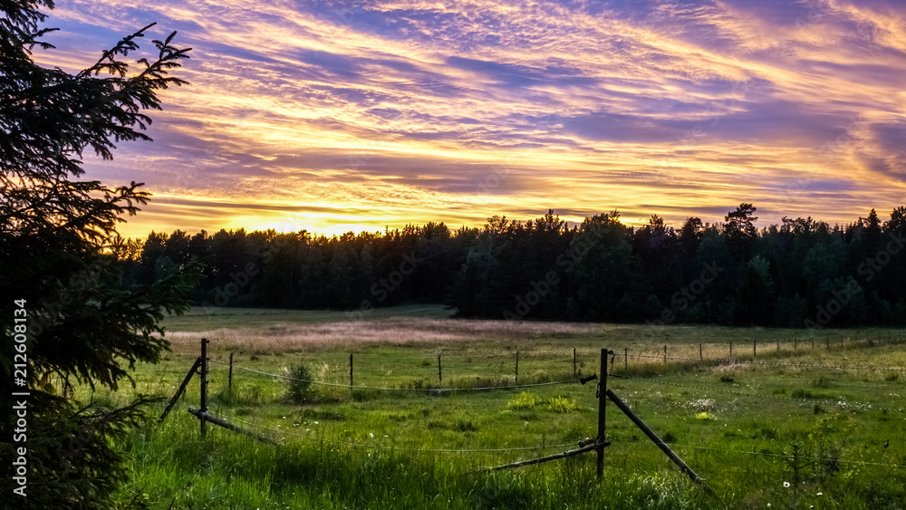 Beautiful, colorful and dramatic sky at sunset. Silhouette of forest and pasture / horse paddock in the foreground.