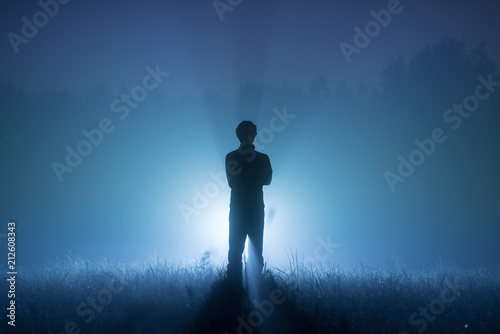 A foggy night. Blue tones. Silhouette of a man. Spotlight behind a man photo