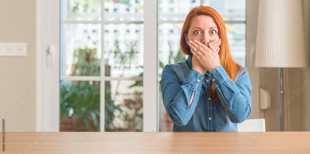 Redhead woman at home shocked covering mouth with hands for mistake. Secret concept.