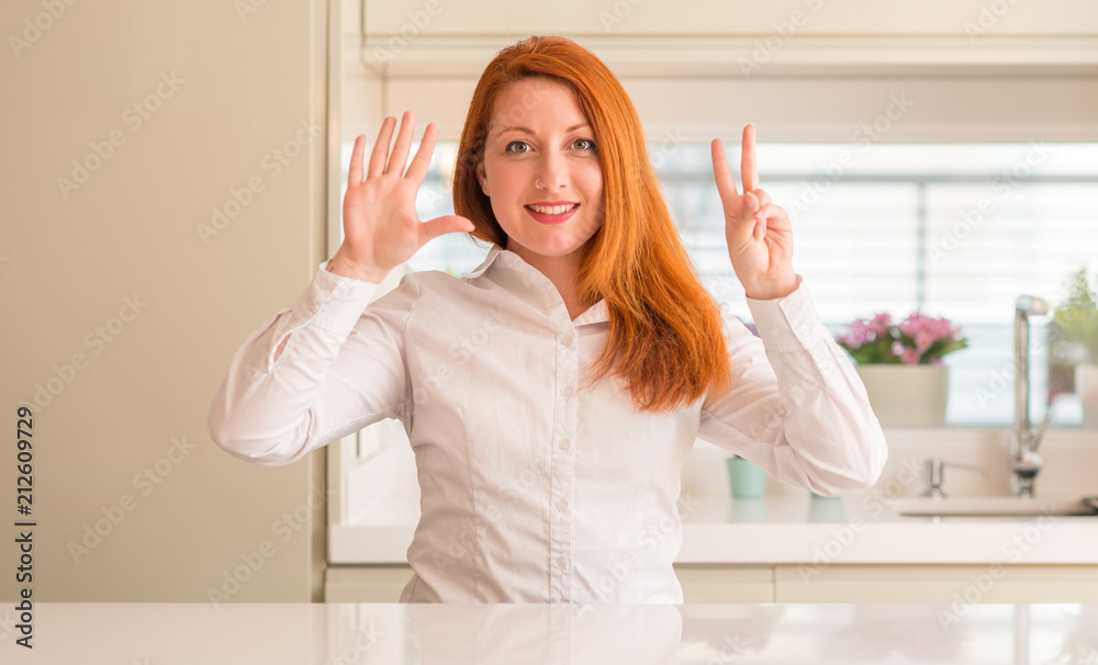 Redhead woman at kitchen showing and pointing up with fingers number seven while smiling confident and happy.