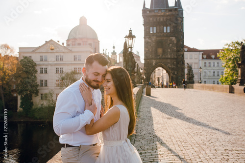 Close up happy groom and bride hugging and smiling while walking on the Charles bridge on sunset. Prague, Czech republic