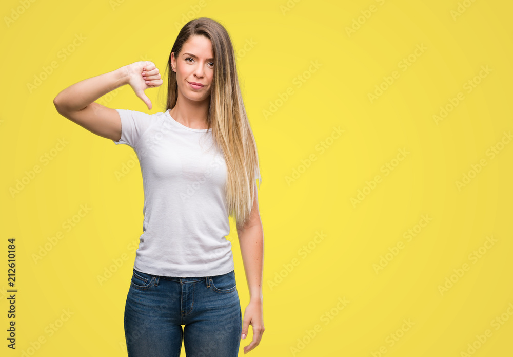 Beautiful young woman wearing t-shirt and jeans with angry face, negative sign showing dislike with thumbs down, rejection concept Beautiful young woman wearing t-shirt and jeans with angry face, negative sign showing dislike with thumbs down, rejection concept