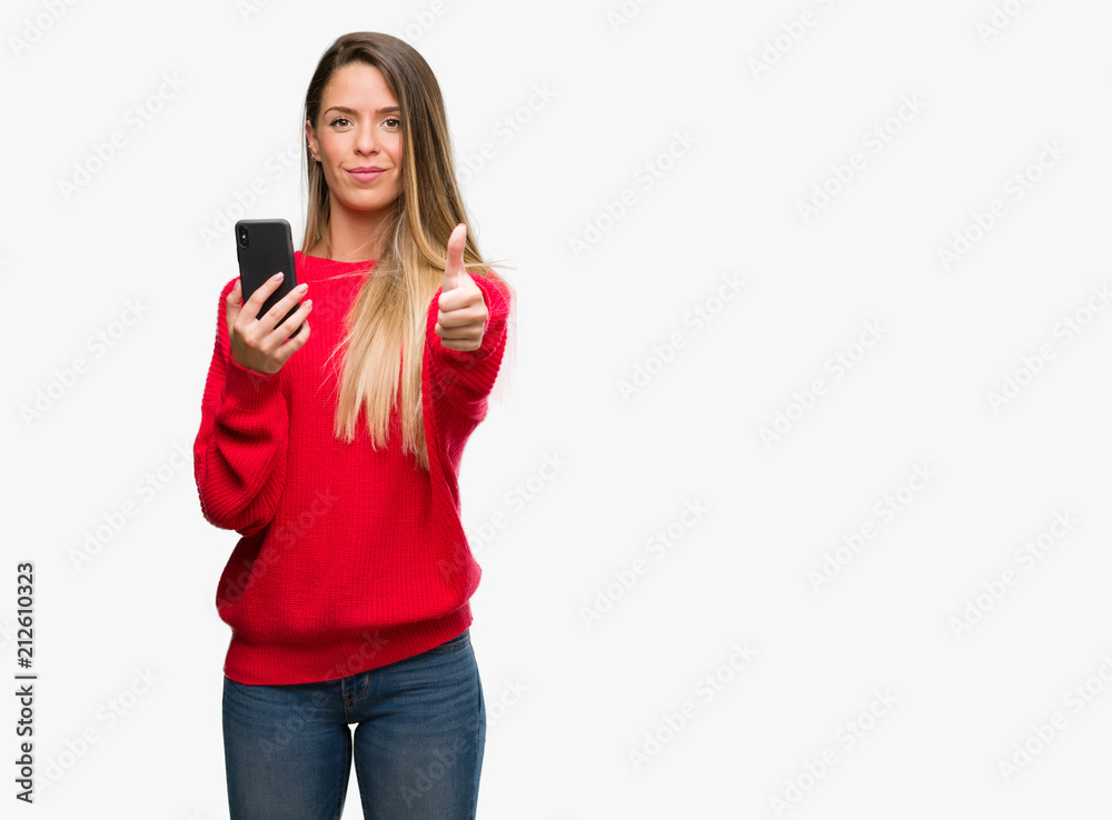 Beautiful young woman using smartphone happy with big smile doing ok sign, thumb up with fingers, excellent sign Beautiful young woman using smartphone happy with big smile doing ok sign, thumb up with fingers, excellent sign
