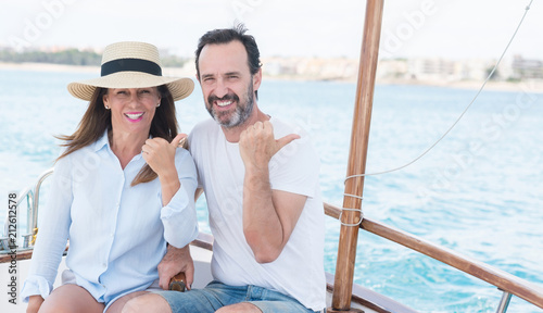 Middle age couple traveling on sailboat pointing with hand and finger up with happy face smiling © Krakenimages.com