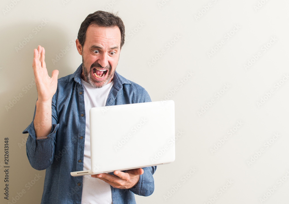 Senior man using laptop computer very happy and excited, winner expression celebrating victory screaming with big smile and raised hands Senior man using laptop computer very happy and excited, winner expression celebrating victory screaming with big smile and raised hands