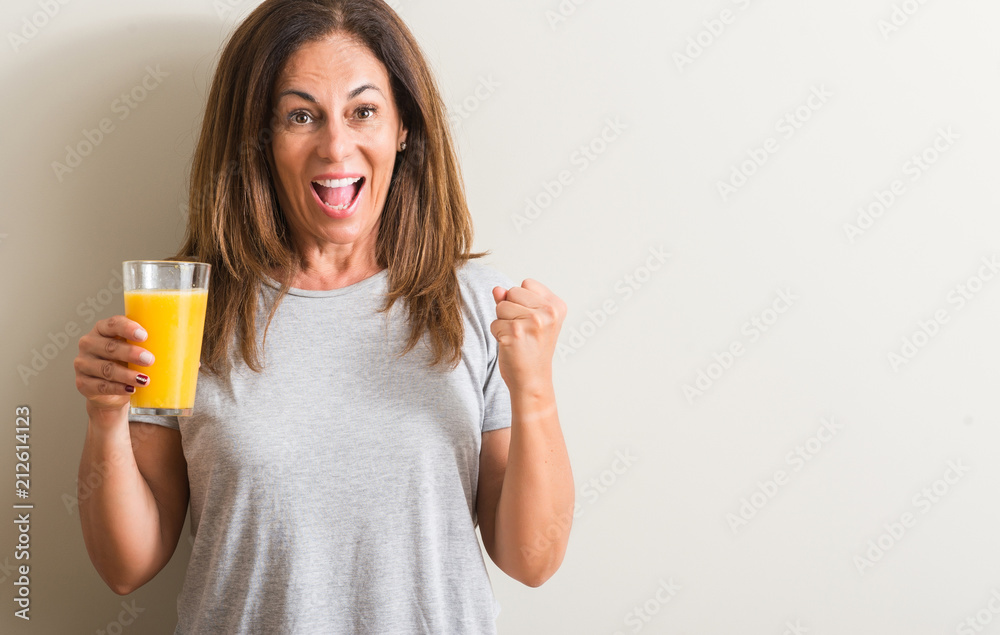 Middle age woman drinking orange juice in a glass screaming proud and celebrating victory and success very excited, cheering emotion Middle age woman drinking orange juice in a glass screaming proud and celebrating victory and success very excited, cheering emotion